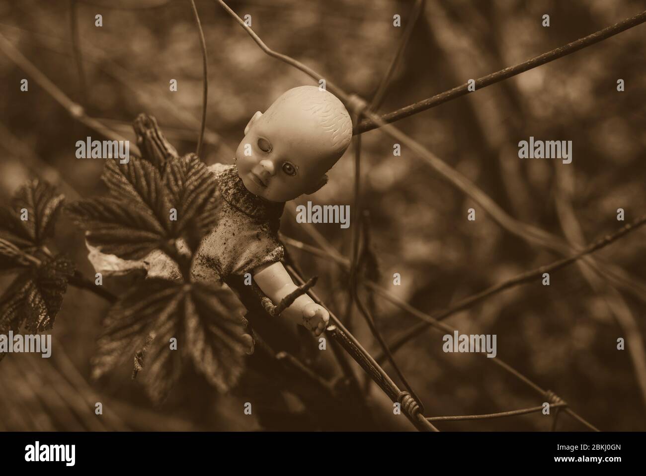Una vecchia bambola sporca si appende su un recinto, bambola del bambino con un solo occhio, bambola creepy, foto in bianco e nero, seppia Foto Stock