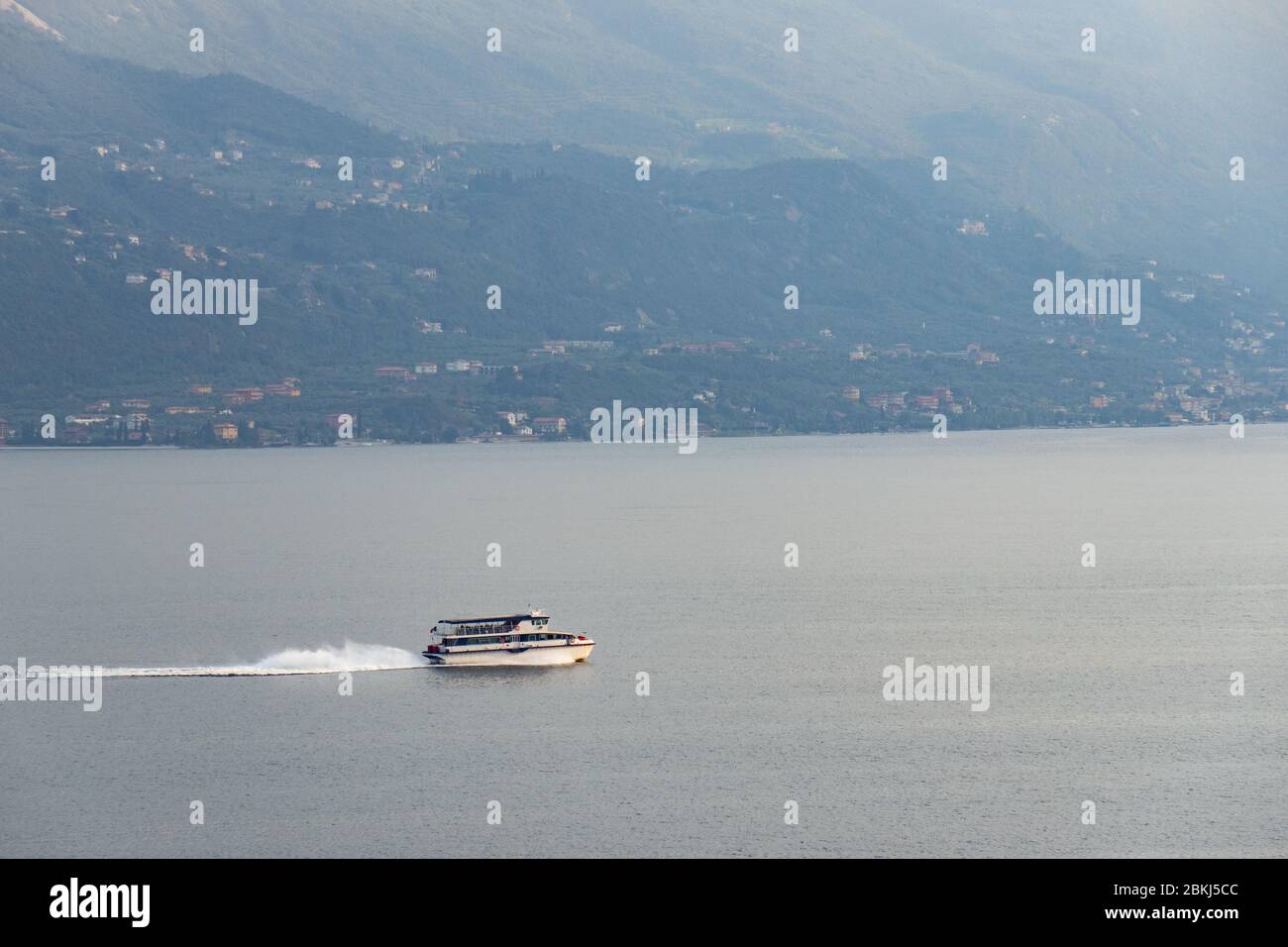 Piccola barca passeggeri che trasporta turisti sul lago di Garda, nel nord Italia. Bel paesaggio sullo sfondo. Foto Stock