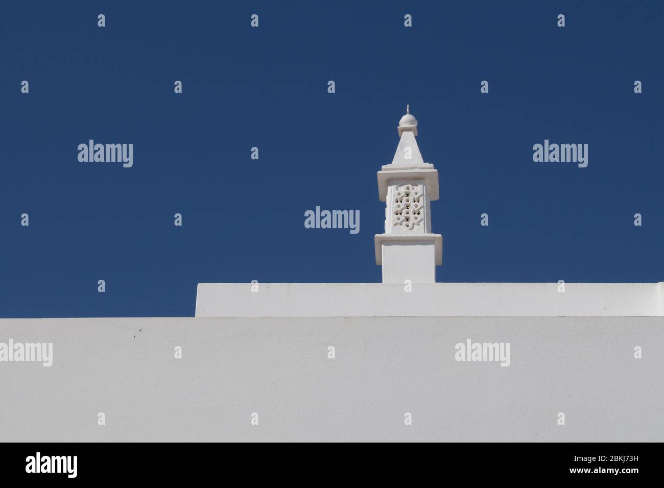 Linee della casa dipinta di bianco con un camino tradizionale portoghese. Cielo blu chiaro. Alvor, Algarve, Portogallo. Foto Stock