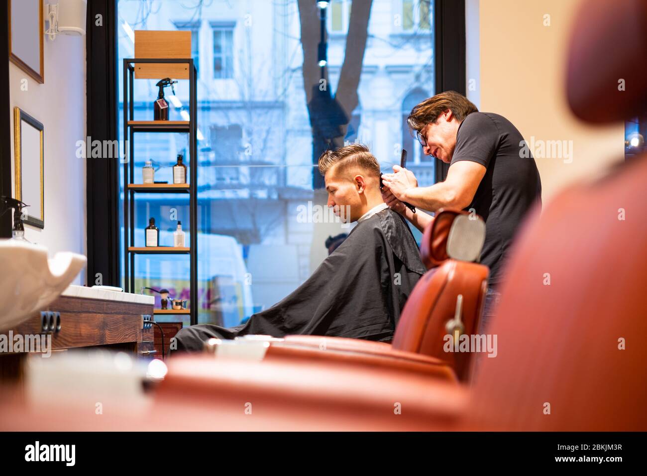 Barber rifinì i capelli di un giovane con un rasoio nel suo barbiere Foto Stock