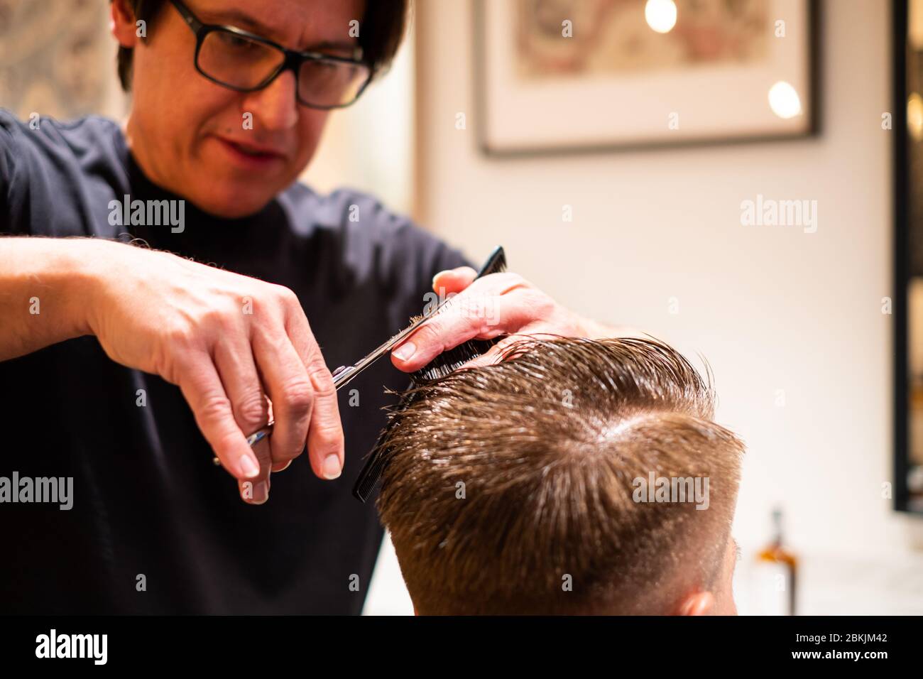 Barber taglia i capelli di un giovane con le forbici e un pettine nel suo barbiere Foto Stock