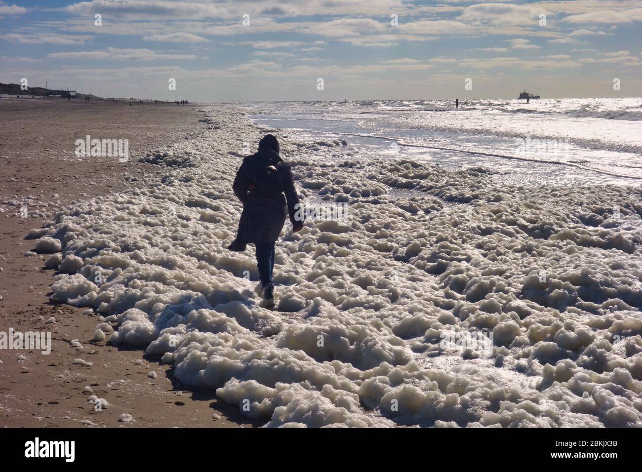 Spiaggia del Mare del Nord con onde, costa e riva. Donna che cammina attraverso l'acqua schiumosa. Foto Stock