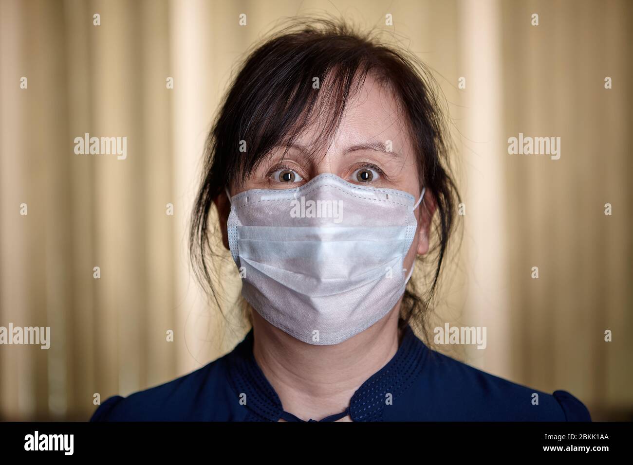 Una donna caucasica di mezza età ha messo in quarantena durante l'epidemia di Covid 19. Femmina bianca in maschera protettiva sul viso autoisolamento in casa sua. Foto Stock