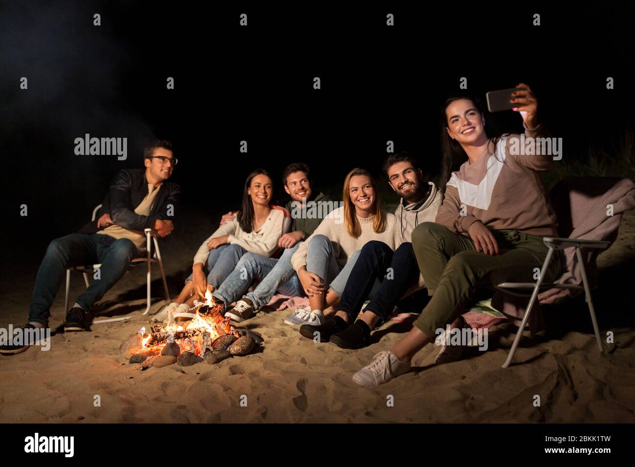 amici felici che prendono selfie al fuoco del campo sulla spiaggia Foto Stock