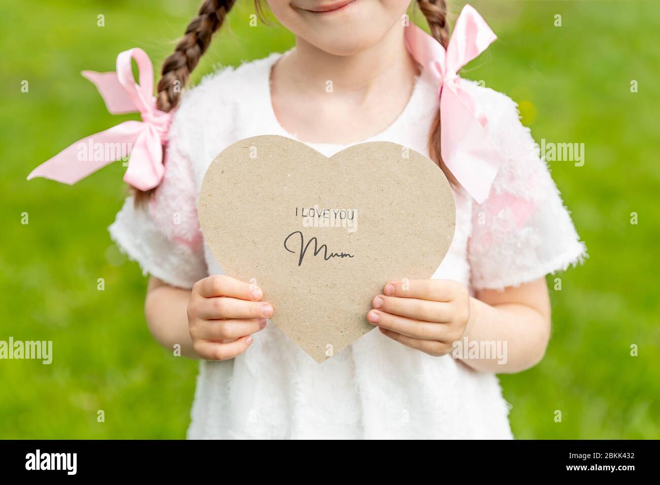 Ti amo mamma scritto su una carta a forma di cuore tenuto da una ragazza su sfondo d'erba Foto Stock