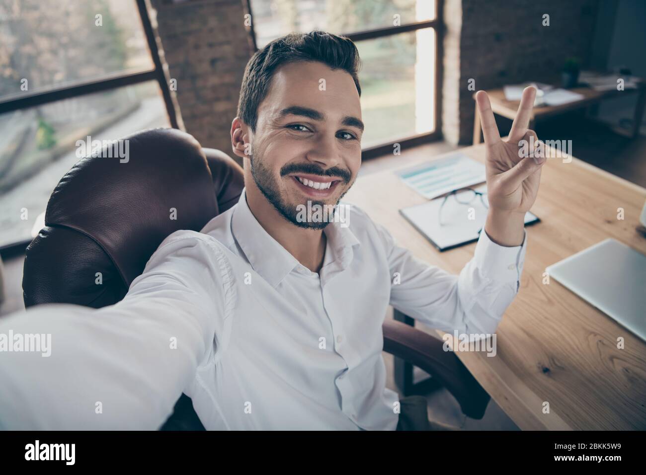 Autoritratto del suo lui bello attraente classe fiducioso allegro uomo barbarare economista consulente avvocato mostrando v-segno al loft moderno Foto Stock