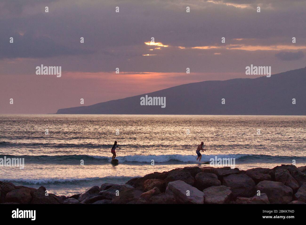 I surfisti silhouette cavalcano l'ultima onda del giorno al tramonto. Foto Stock