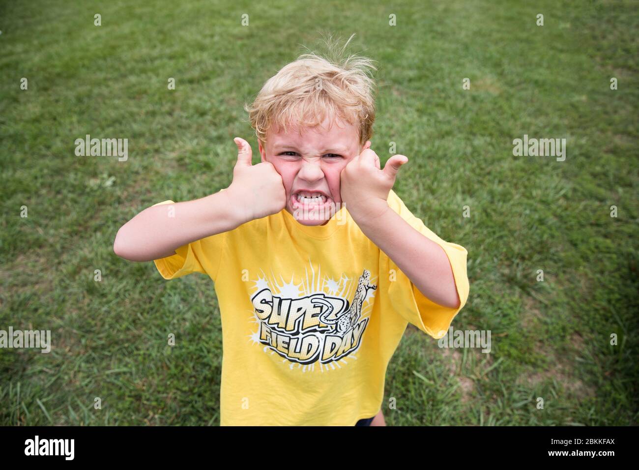 Silly Blonde Boy schizza la faccia con due pollice alla scuola Field Day Foto Stock