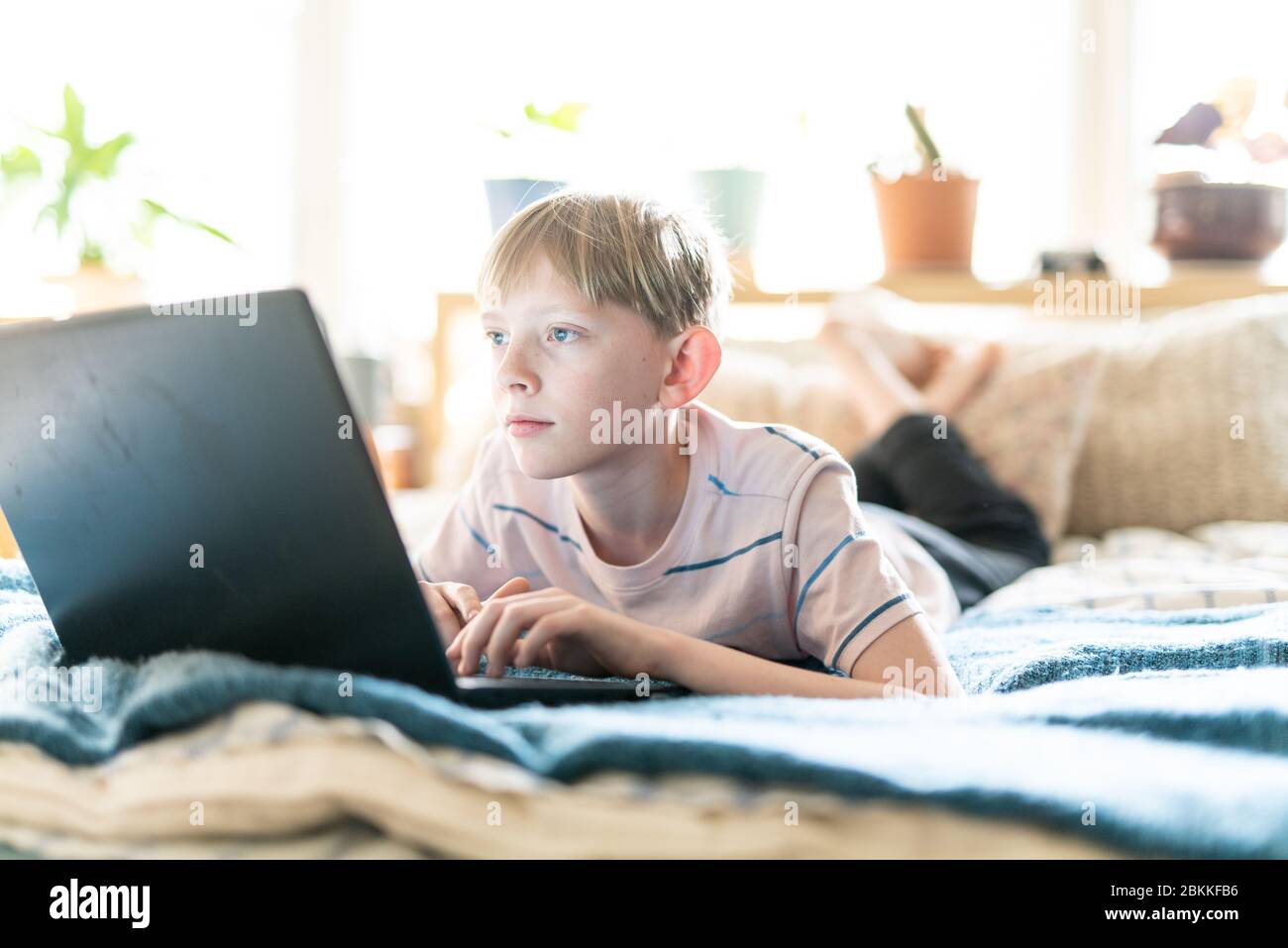 Ragazzo teenager che lavora su un computer portatile mentre si sdraia sul letto spazio luminoso Foto Stock