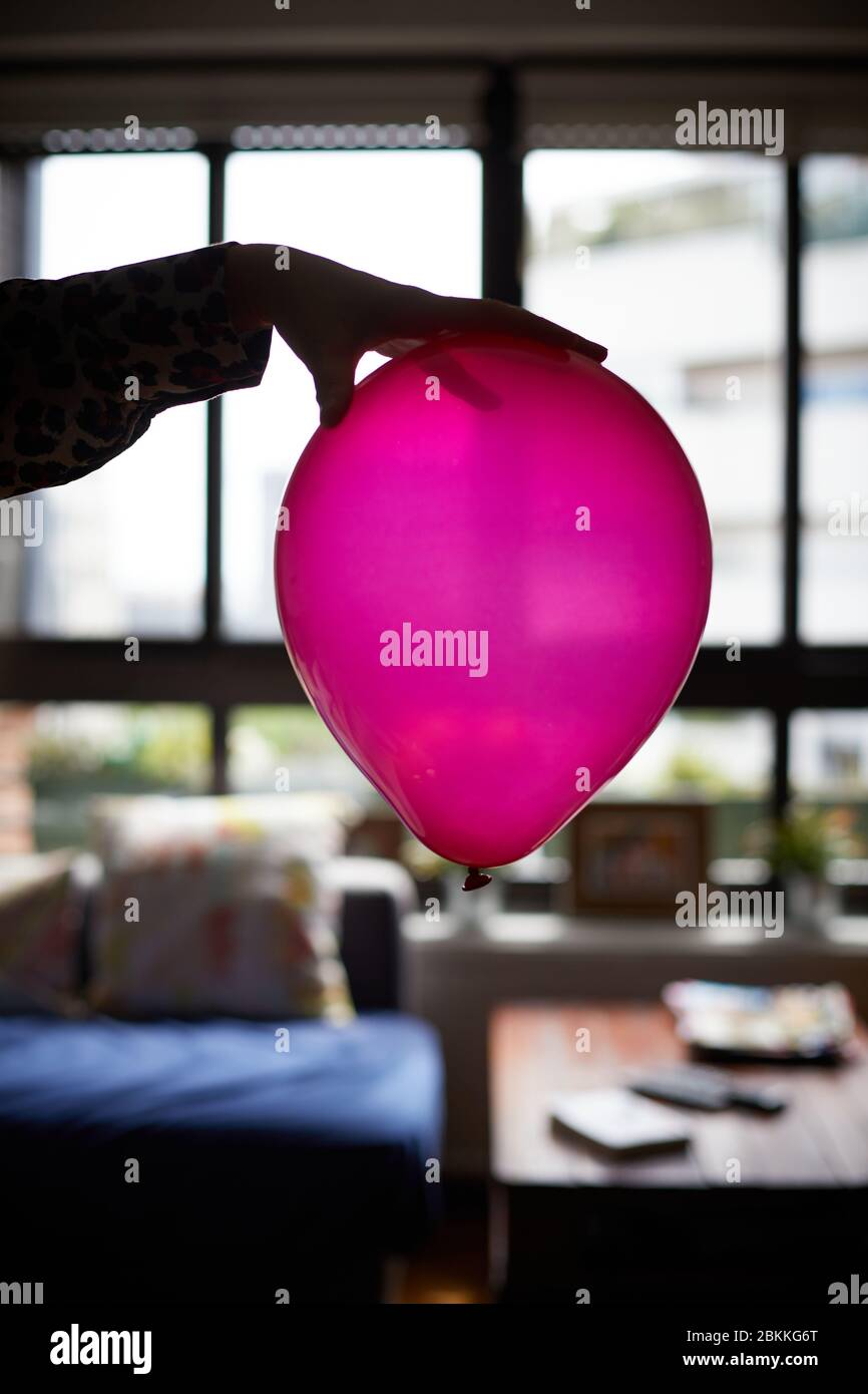 La mano di una donna tiene un palloncino rosa a casa. Foto Stock
