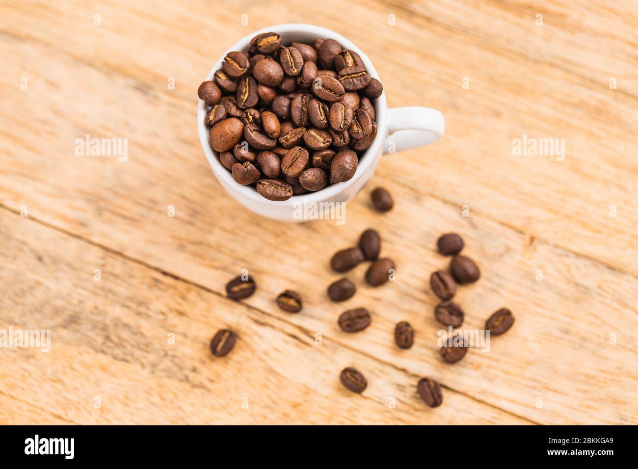 Una tazza bianca piena di chicchi di caffè marroni su un tavolo di legno Foto Stock