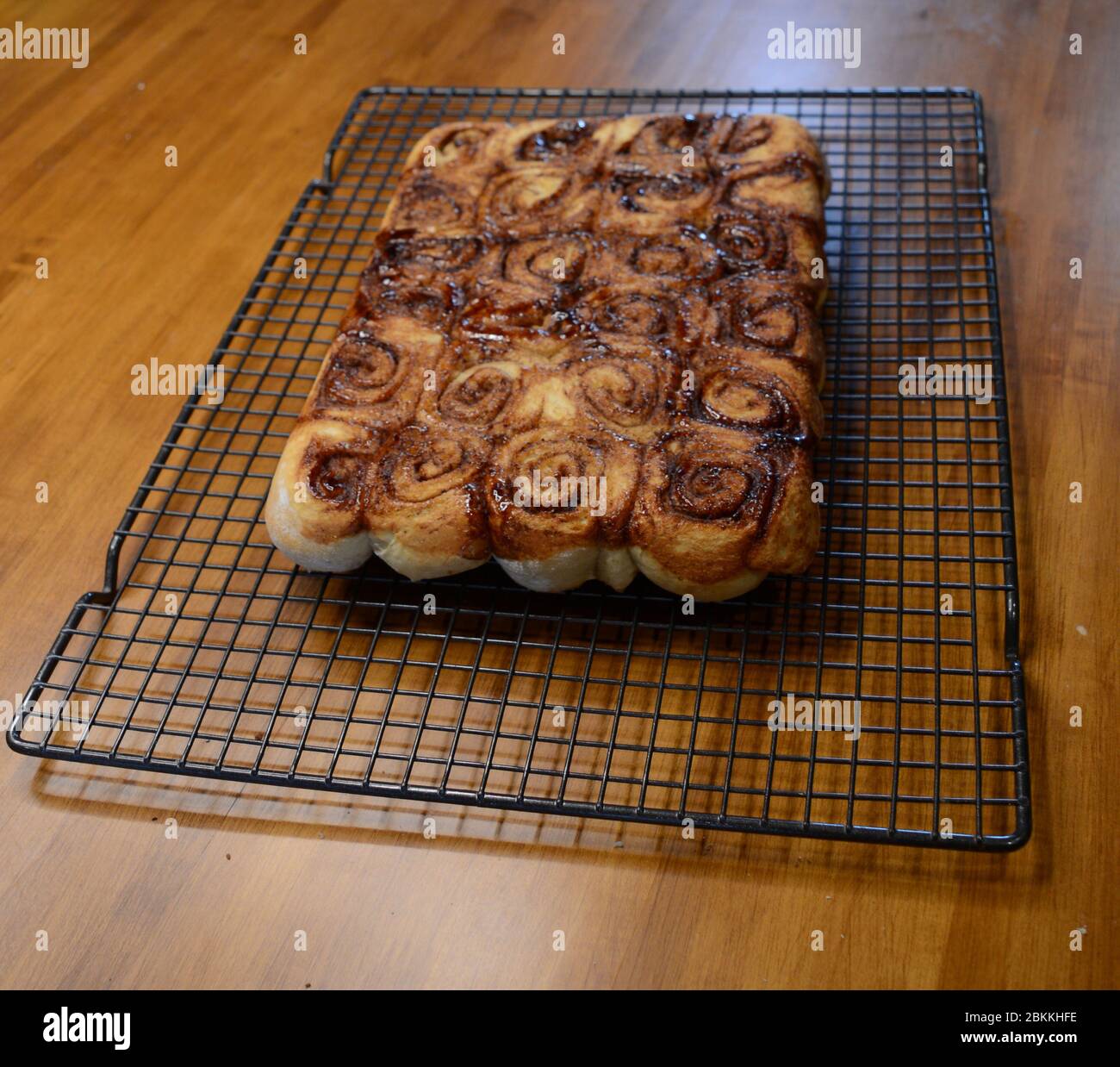 Una vista di dolci di cannella appena sfornati che si raffreddano su una rastrelliera di filo in attesa di essere glassato Foto Stock