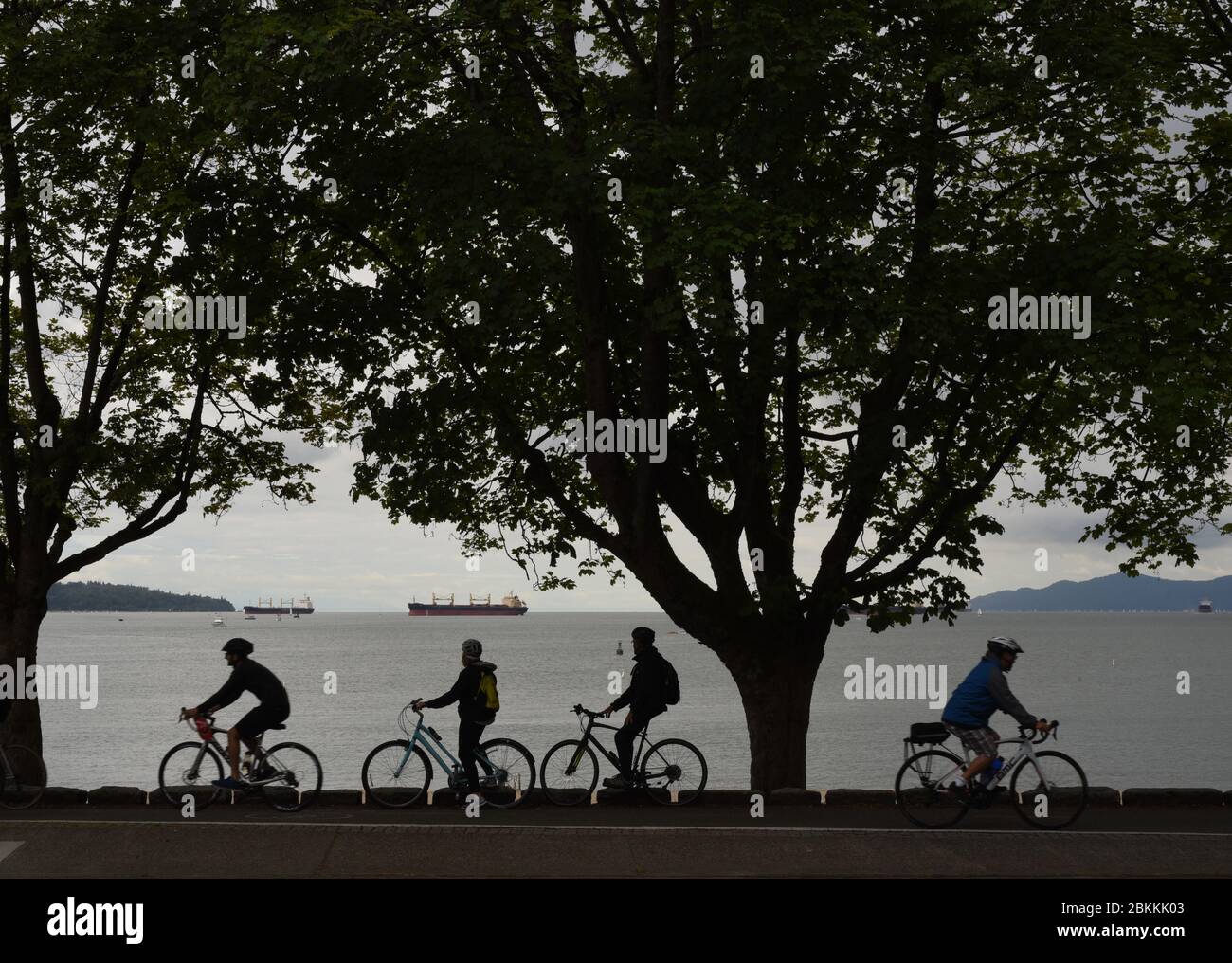 I ciclisti che indossano le biciclette sono silhoueted mentre ammirano la English Bay e i freighter ancorati mentre prendono l'advanatge delle piste ciclabili per recrea Foto Stock
