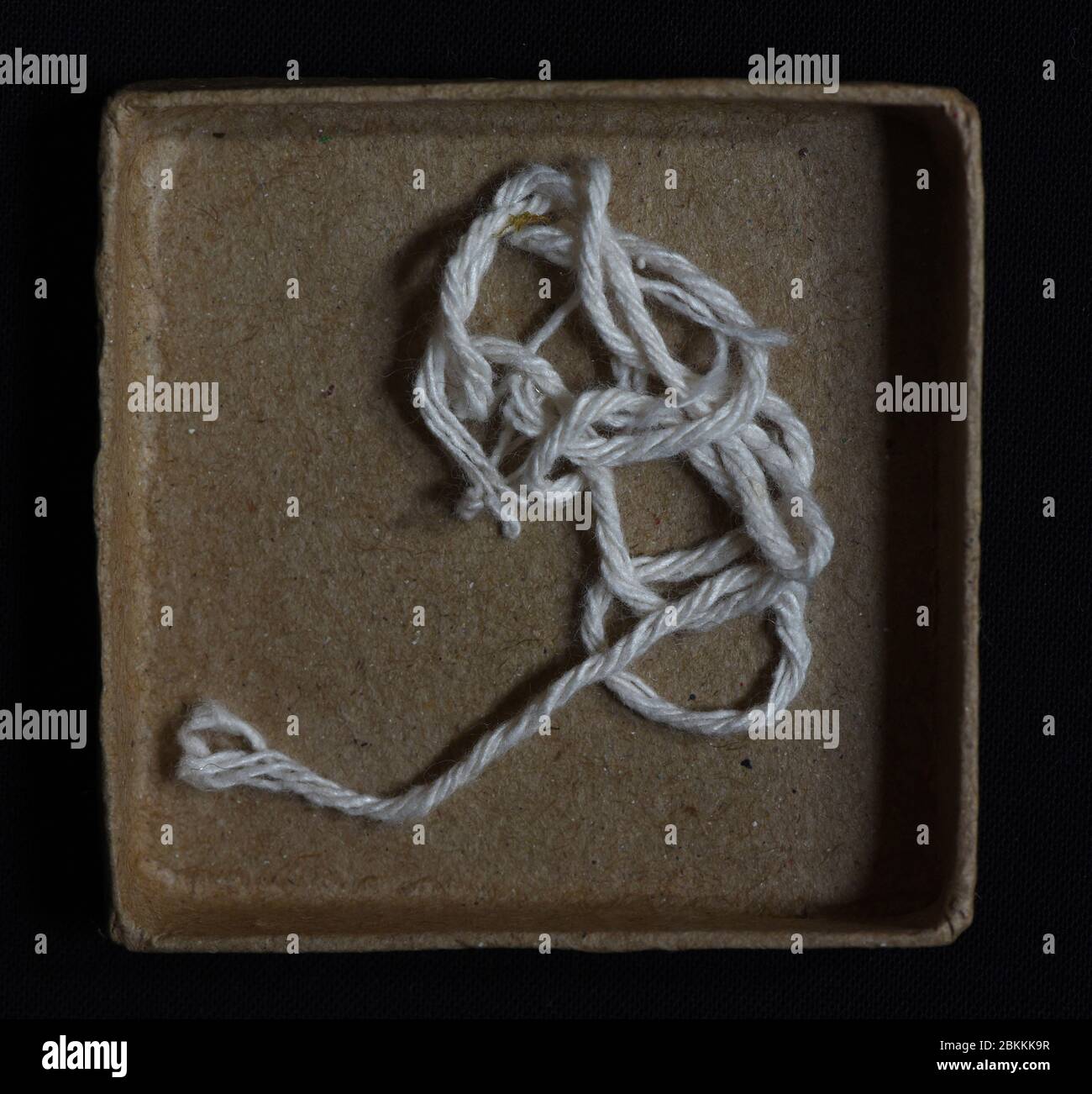 I fili di spago bianco si sfrangiano e si sfilano all'interno di una piccola scatola di cartone Foto Stock