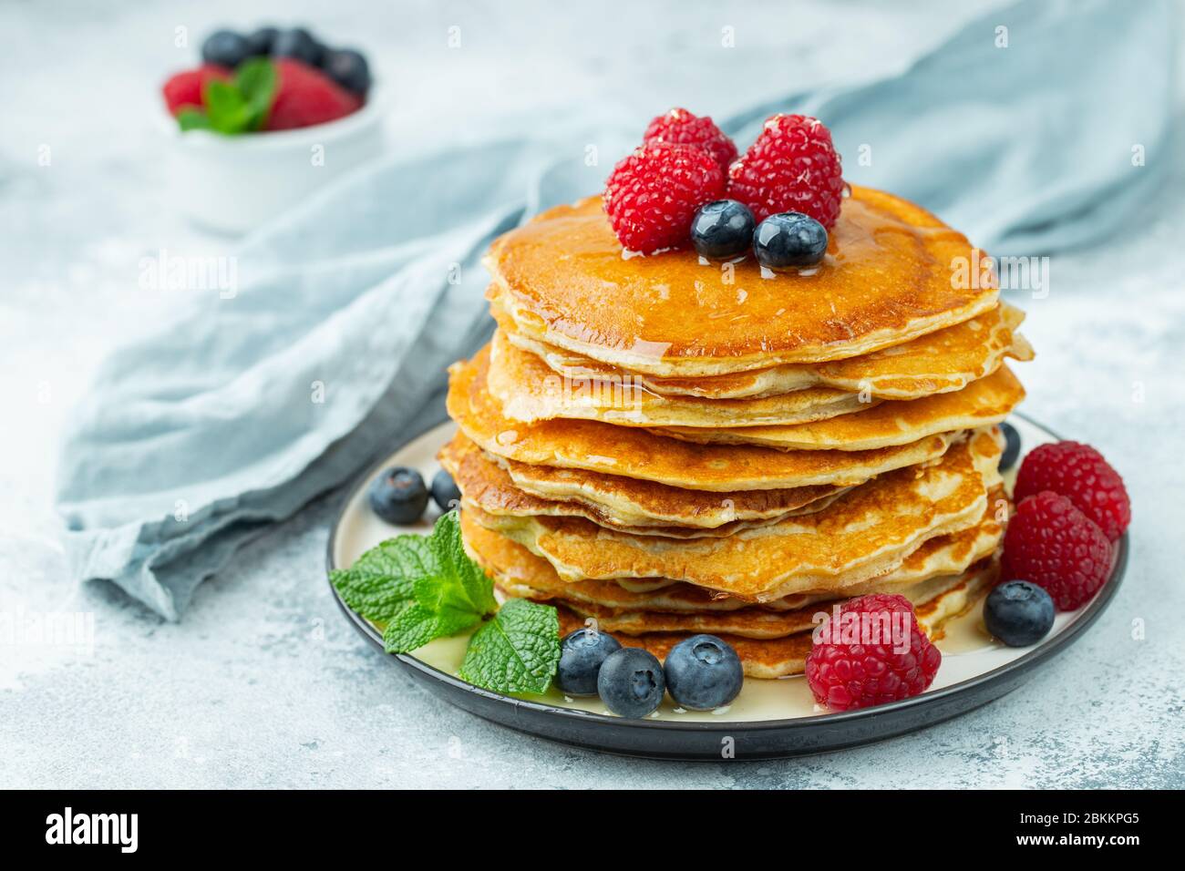 Primo piano deliziosi pancake, con mirtilli freschi, lamponi e miele su uno sfondo chiaro Foto Stock