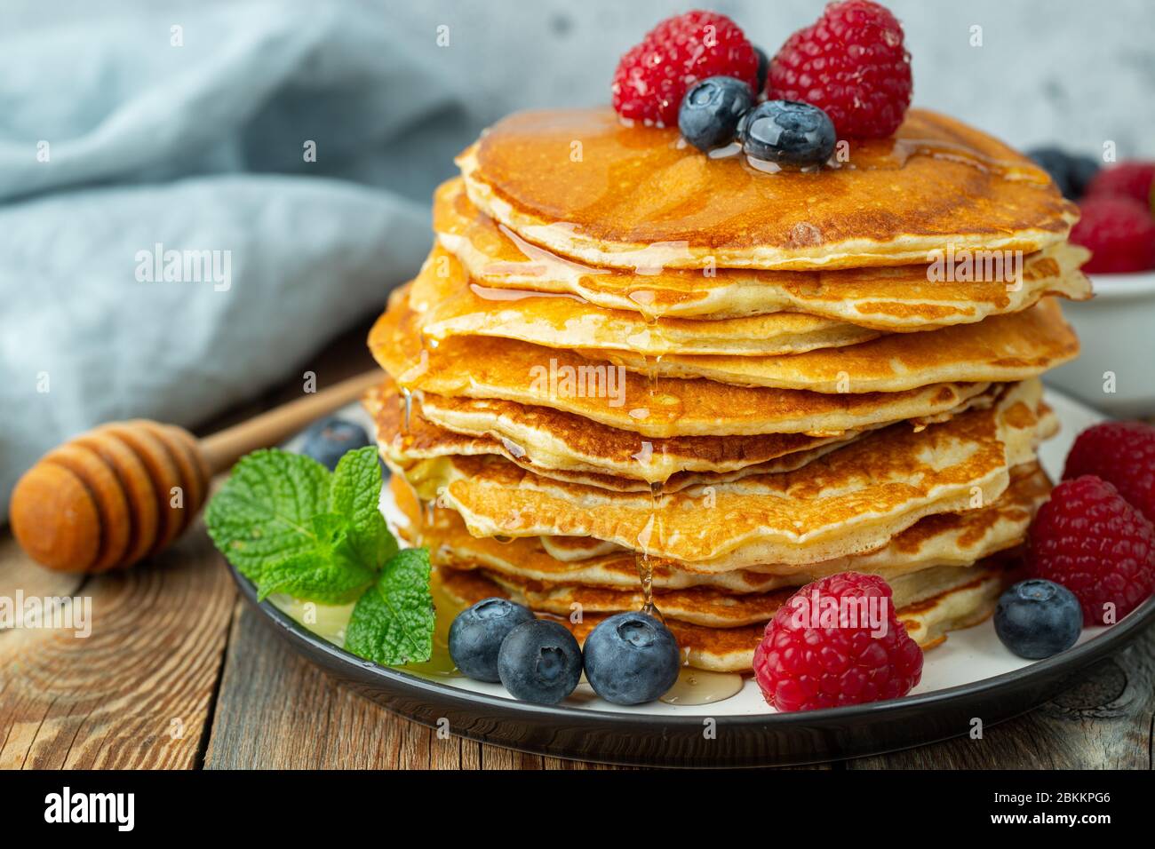 Primo piano deliziosi pancake, con mirtilli freschi, lamponi e miele su uno sfondo chiaro Foto Stock