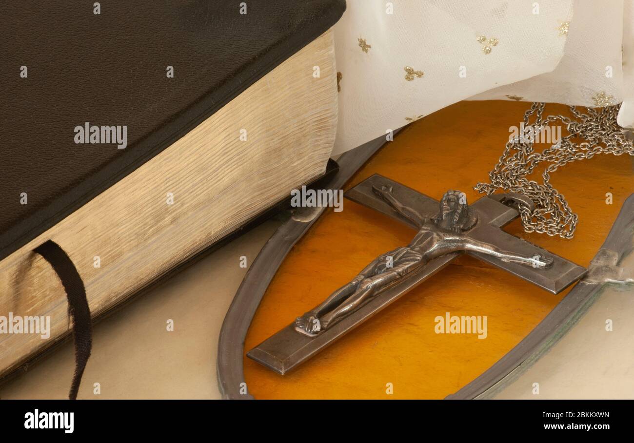 Primo piano che mostra un grande crocifisso sulla catena con sfondo di vetro colorato d'oro accanto ad una Bibbia chiusa con sfondo bianco stella indicativo del cielo. Foto Stock