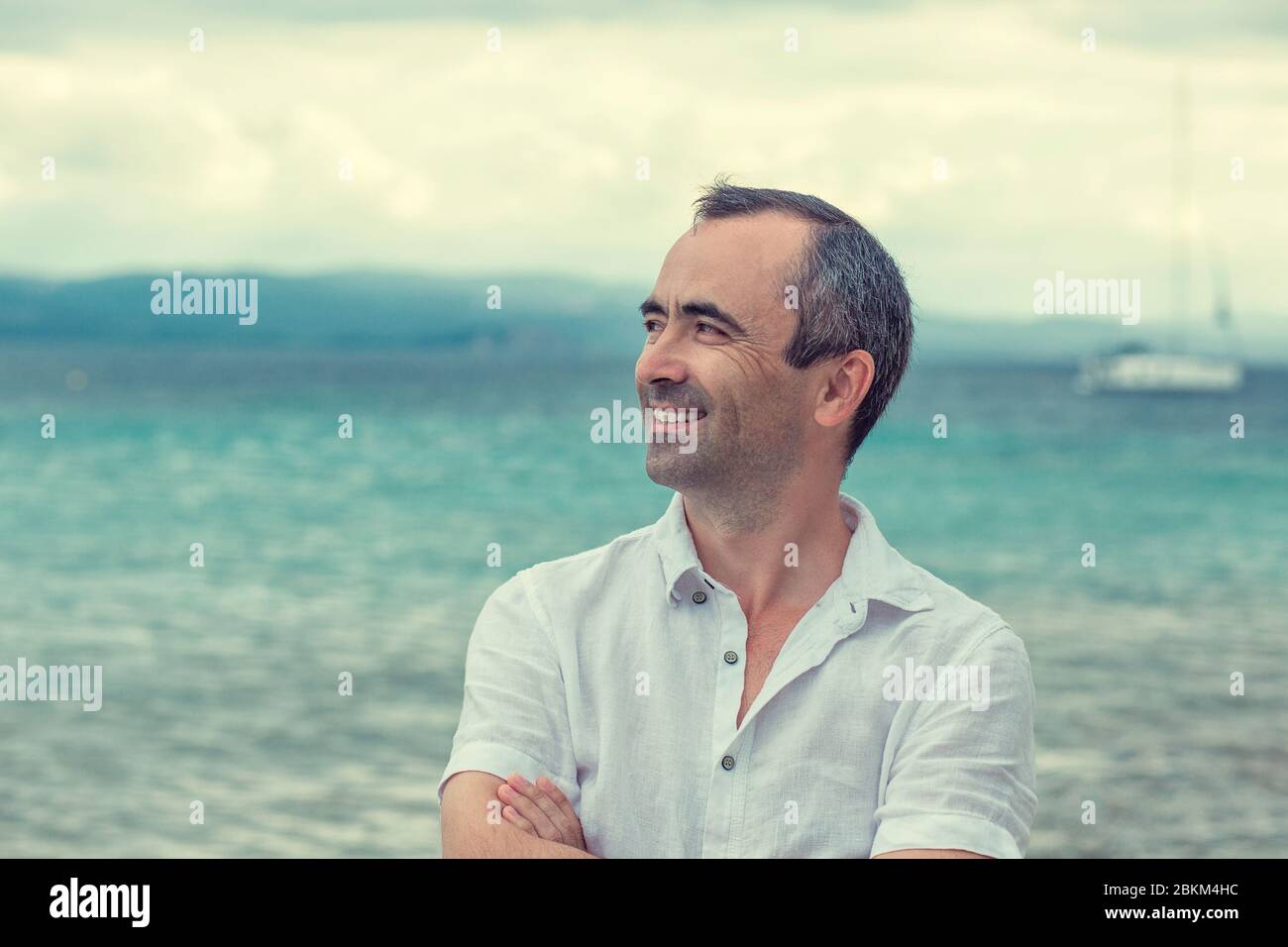 Uomo sorridente a profilo laterale con braccia incrociate dal mare, sorriso soothy uomo di mezza età multiculturale razza mista Foto Stock