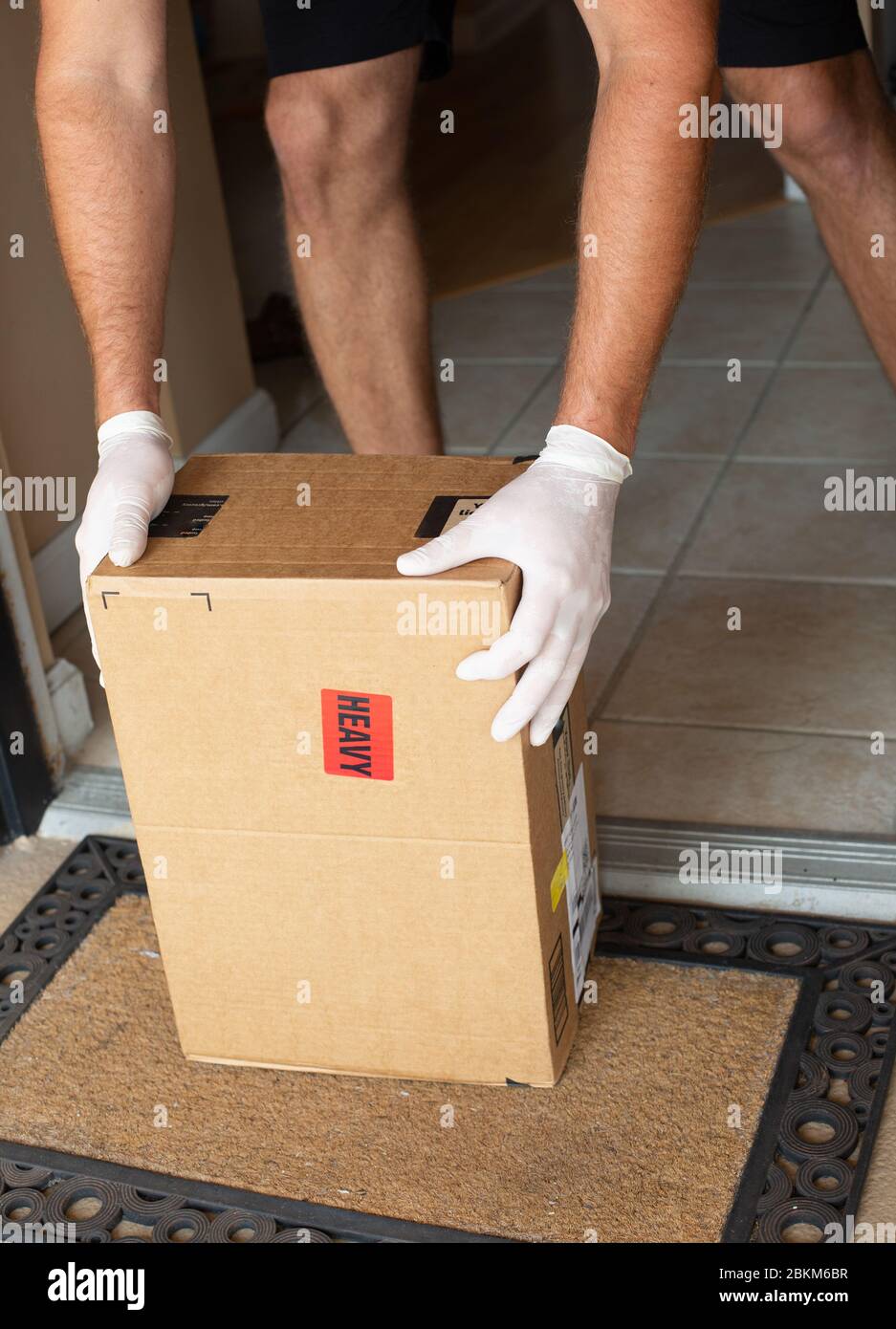 Doorsteppackage in mano alla porta dell'appartamento. Quarantena dovuta a coronavirus. Concetto di fornitura del servizio. Foto Stock