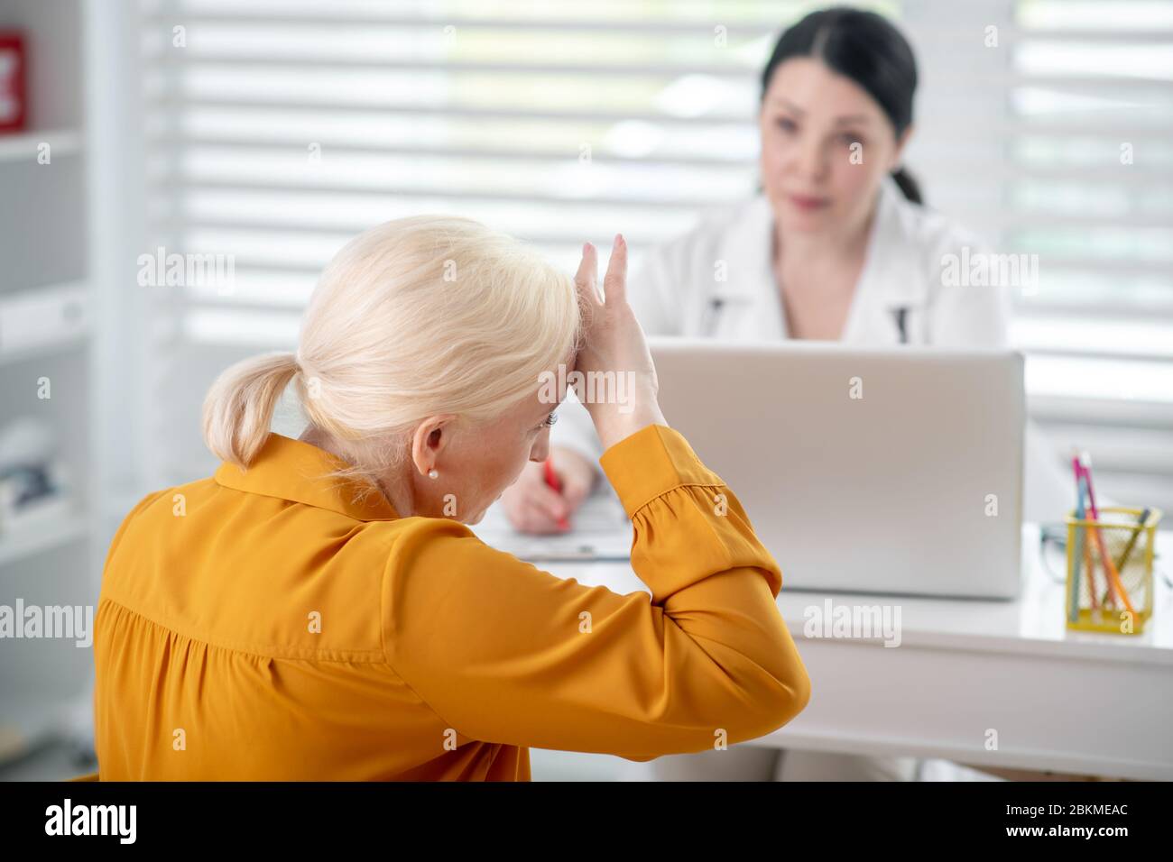 Donna in cappotto bianco che guarda paziente in giallo. Foto Stock
