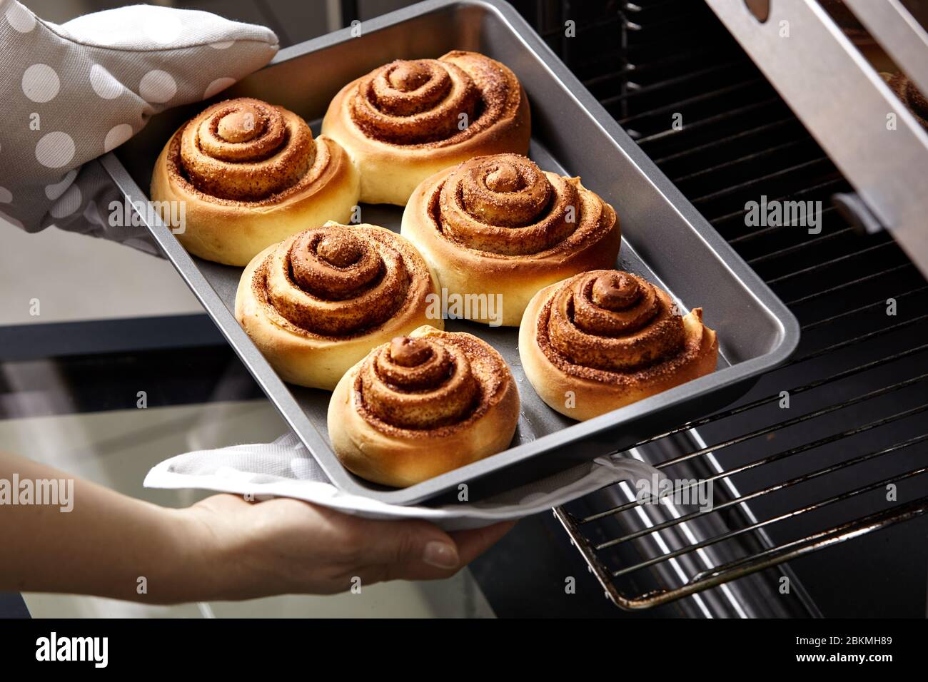 Una donna toglie i cinabon freschi dal forno. I rotoli di cannella vengono cotti nel forno. Cottura fatta in casa. Foto Stock