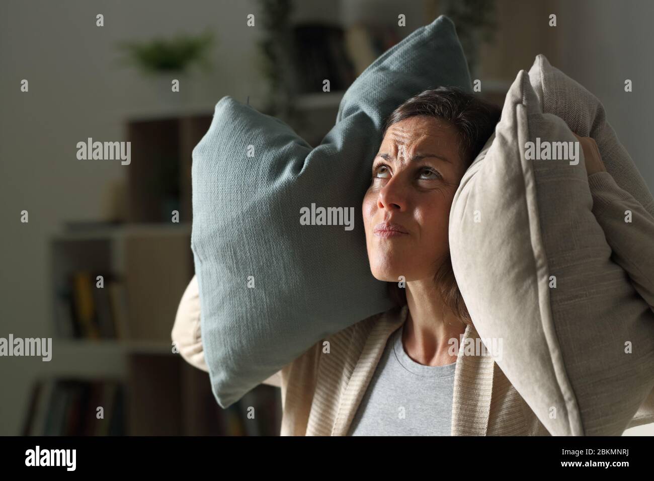 Donna adulta seccata che soffre di rumore vicino nel soggiorno di notte a casa Foto Stock