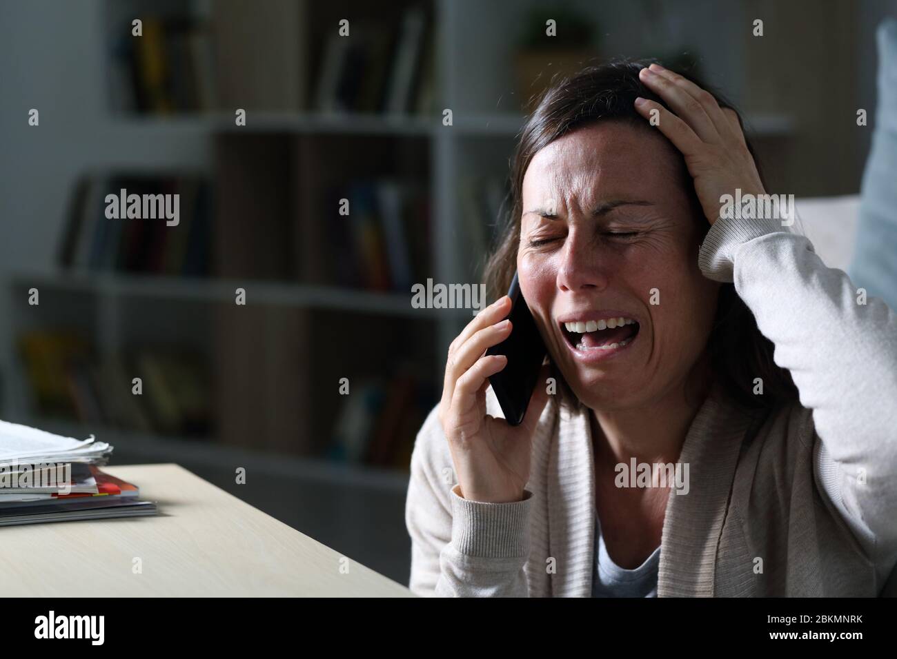 Donna adulta triste che chiama sullo smartphone piangendo seduto sul pavimento di notte a casa Foto Stock