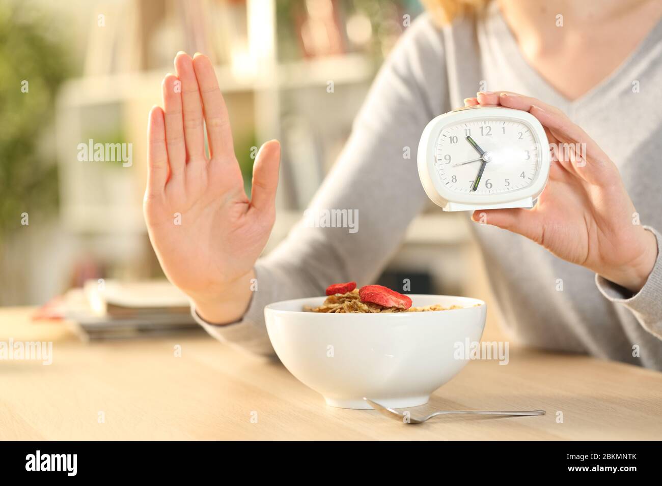 Primo piano delle mani della donna sul digiuno intermittente facendo stop segno di attesa prima di mangiare ciotola di cereali su un tavolo a casa Foto Stock