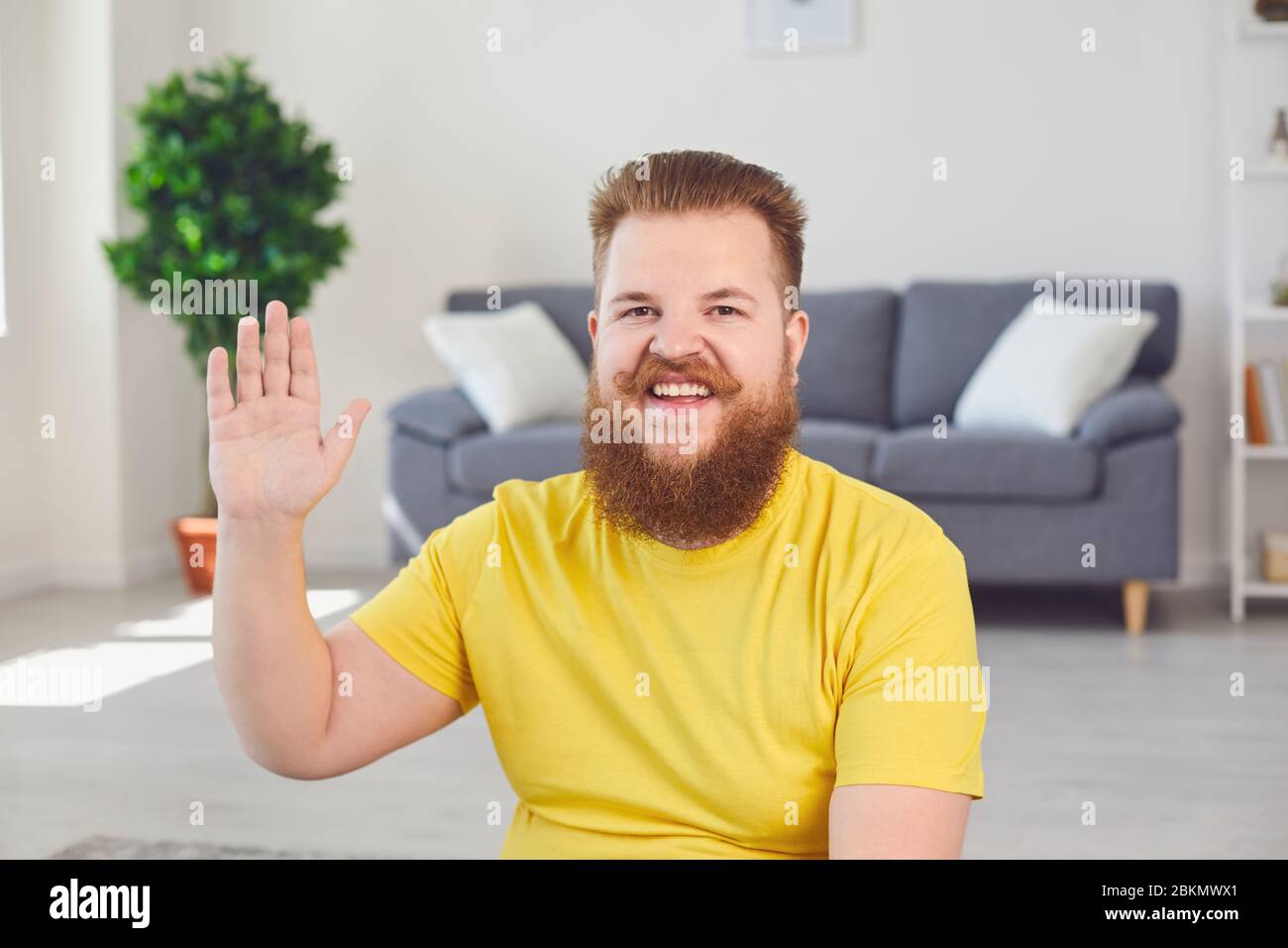 Videochiamata in conferenza online. L'uomo bearded del maschio divertente sorride guarda la macchina fotografica nella stanza all'ufficio domestico. Foto Stock
