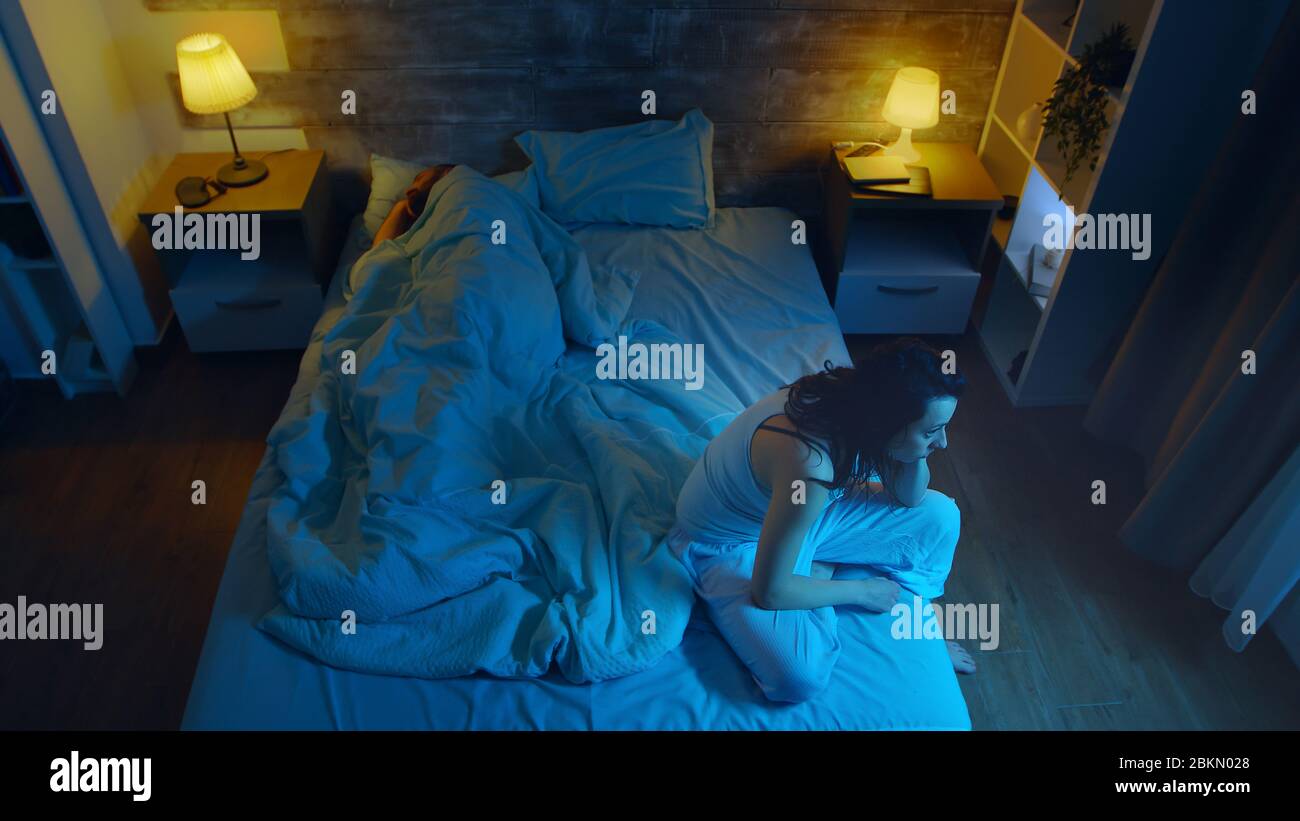 Giovane donna che soffre di insonnia mentre suo marito dorme. Camera con luce sulla luna. Foto Stock
