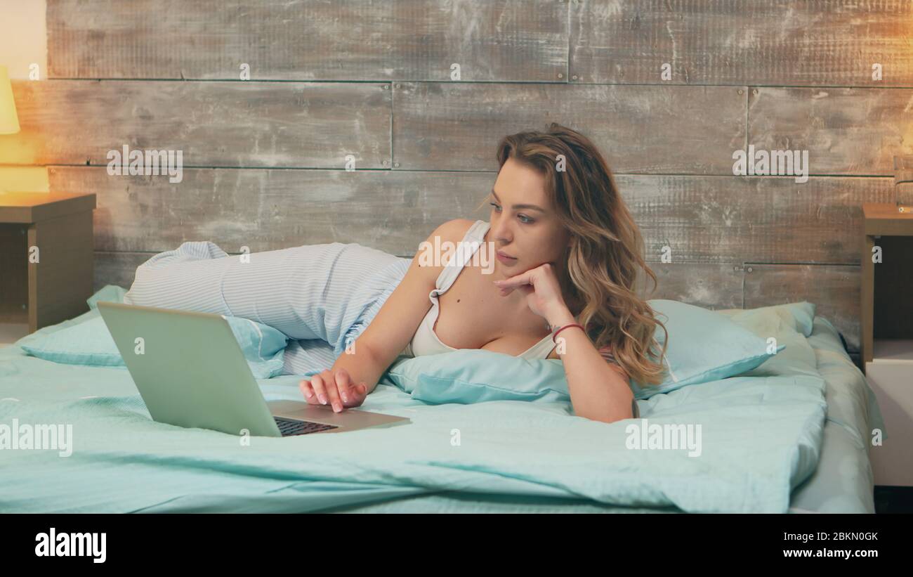 Zoom indietro scatto di bella donna che indossa pigiama di lavoro sul laptop prima di andare a dormire. Buon cane. Foto Stock
