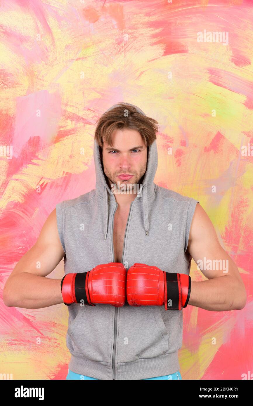 Sport e combattere il concetto. Uomo con disordinati capelli arancione su sfondo di texture. Boxer con faccia grave treni. Ragazzo in grigio felpa con cappuccio senza maniche rosso indossa le Foto sto...