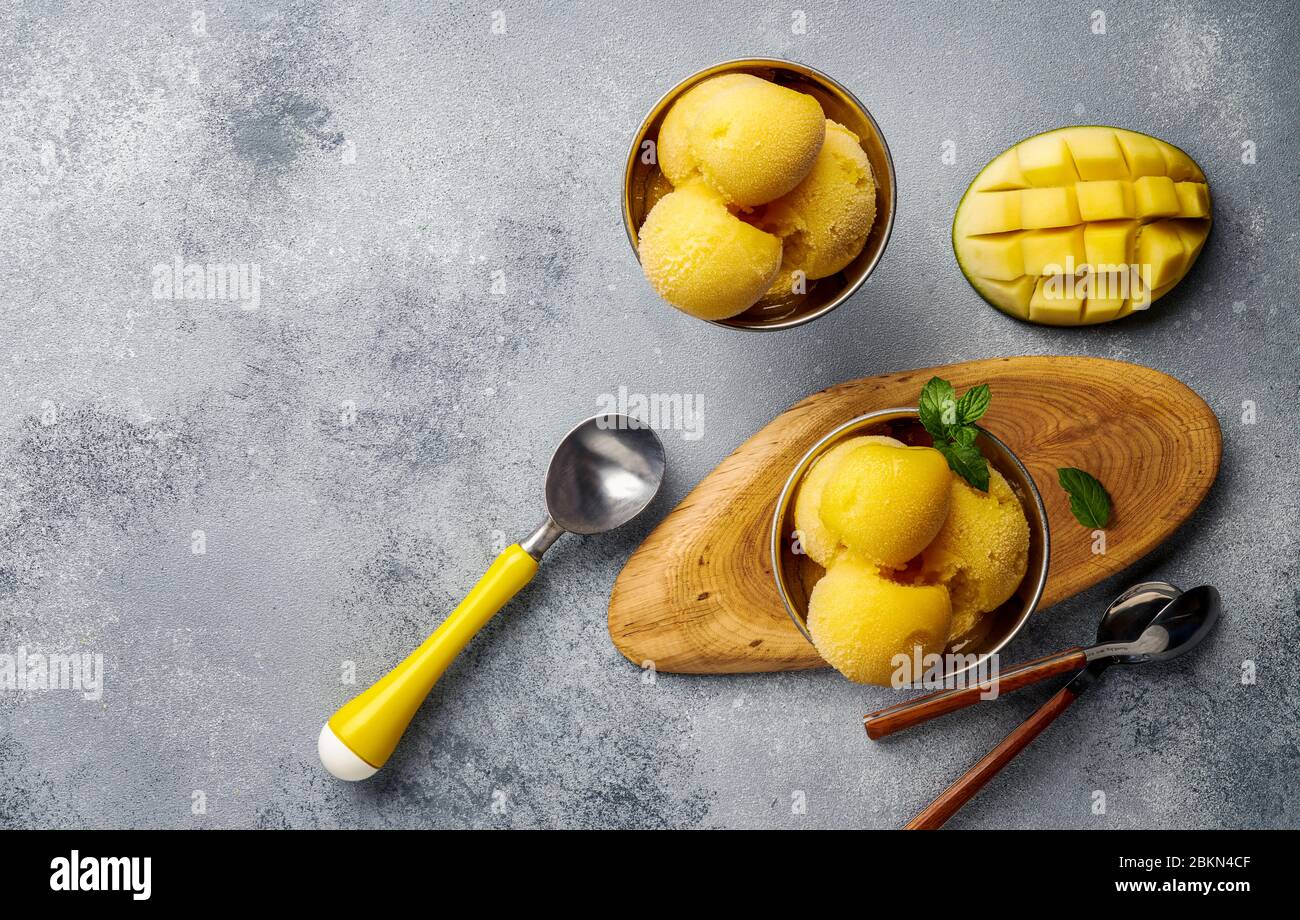 Gelato Mango su fondo grigio cemento. Spazio di copia. Vista dall'alto delle fette di mango e del gelato in ciotola. Foto Stock