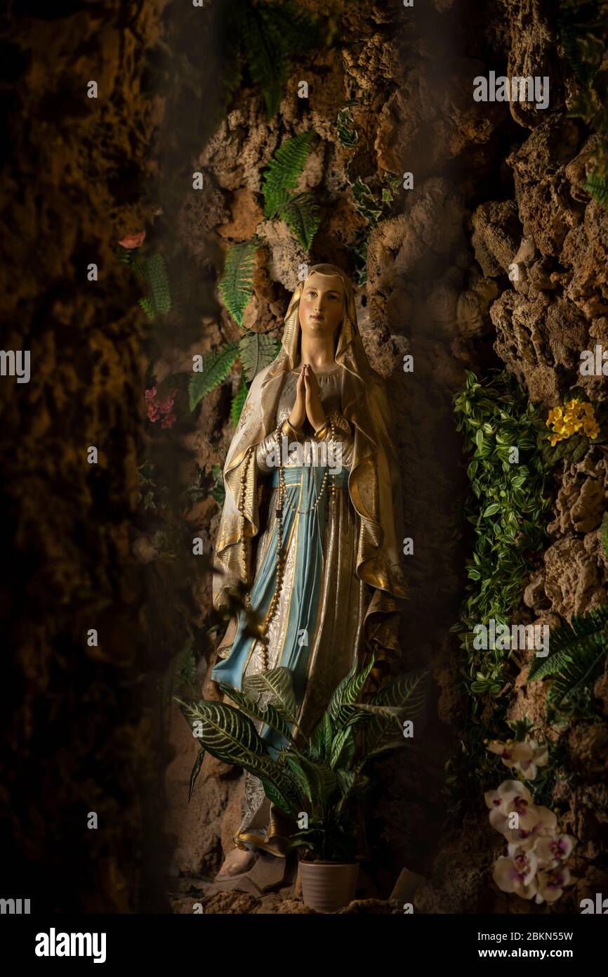 Una statua della Madonna che prega nella chiesa dei gesuiti nella città vecchia di Dubrovnik, Dalmazia, Croazia. È circondata da rocce e vegetazione Foto Stock