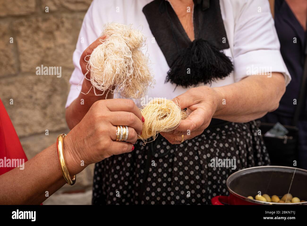 Una donna che indossa un tradizionale vecchio costume folcloristico che mostra alla gente come il filato di seta viene prodotto in un ambiente rustico e autentico Foto Stock