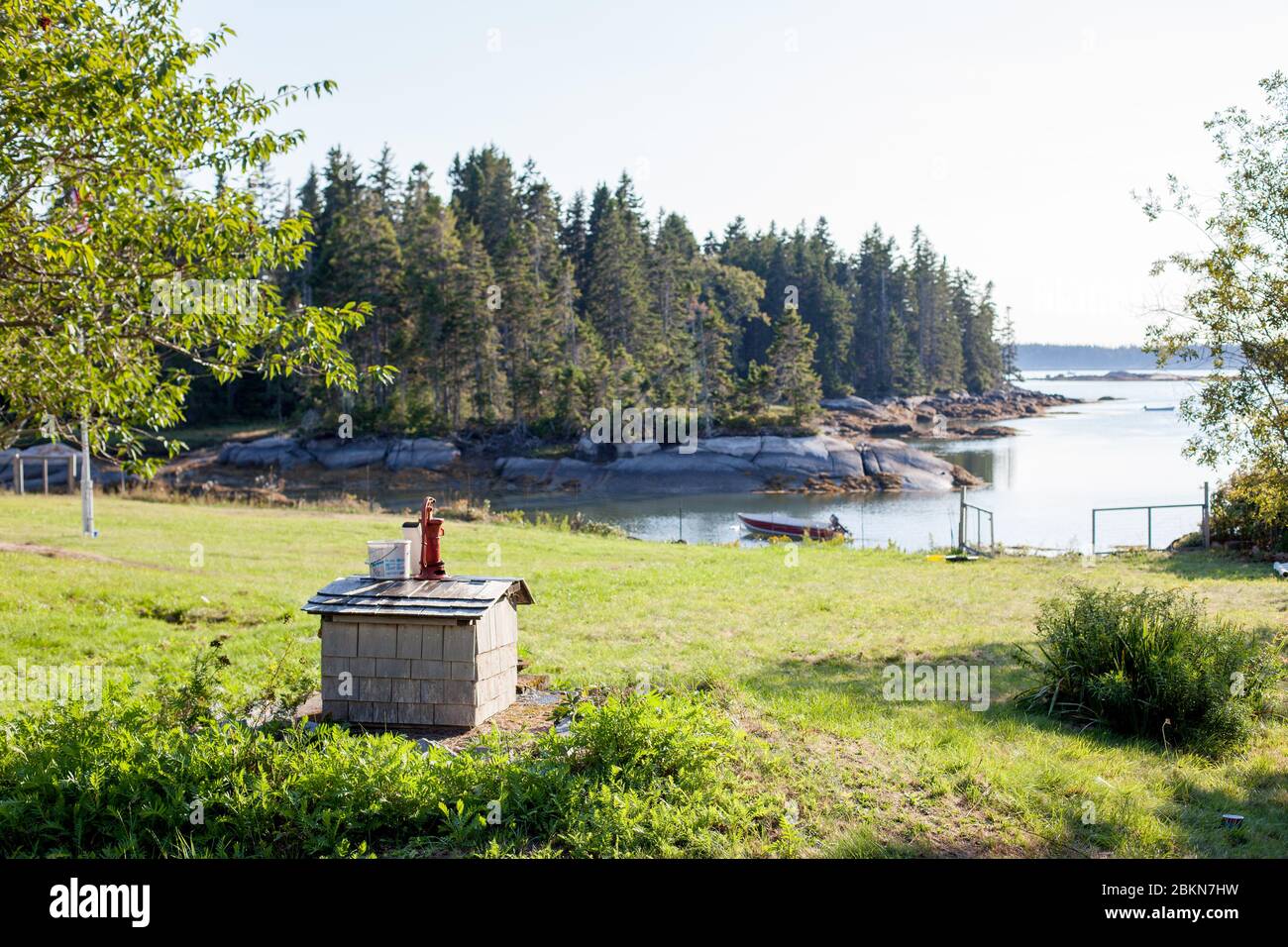 Una piccola casa con una pompa rossa si trova sul bordo di un prato, con una baia e alberi sempreverdi sullo sfondo, a Vinalhaven, Maine, USA Foto Stock