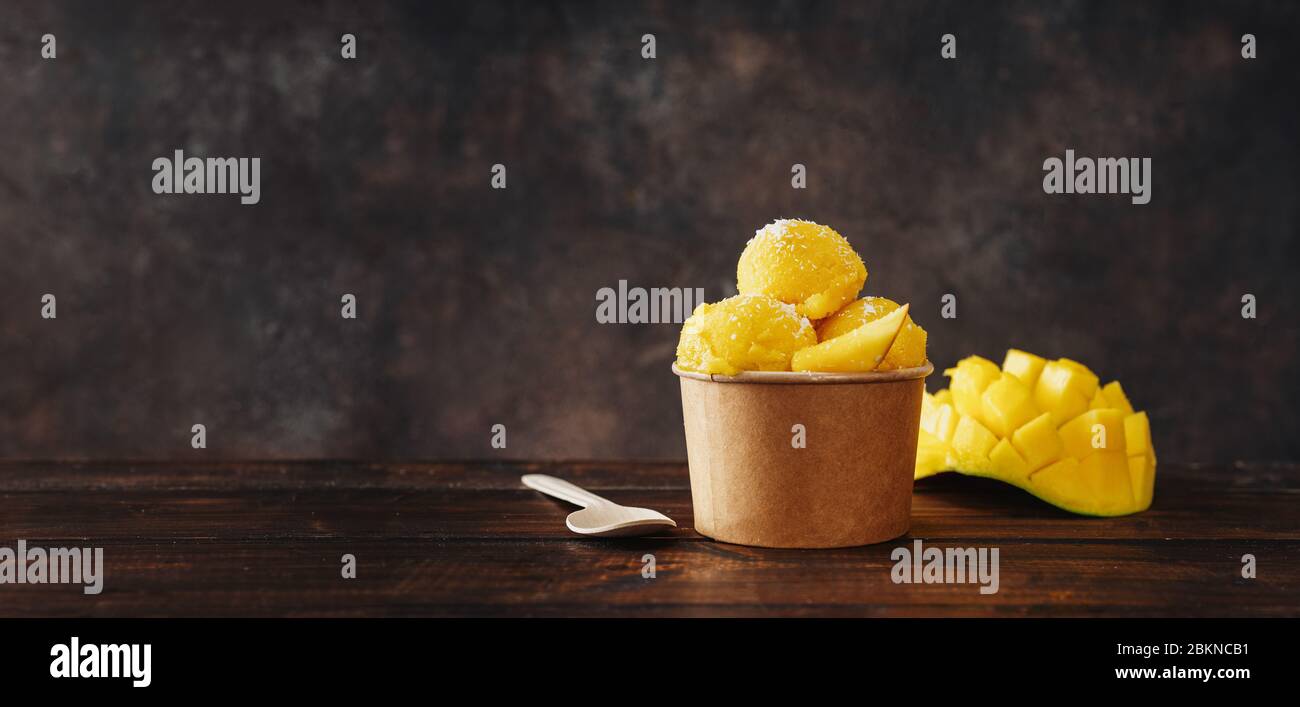 Delizioso sorbetto al mango vegano in una tazza di carta artigianale su sfondo scuro Foto Stock