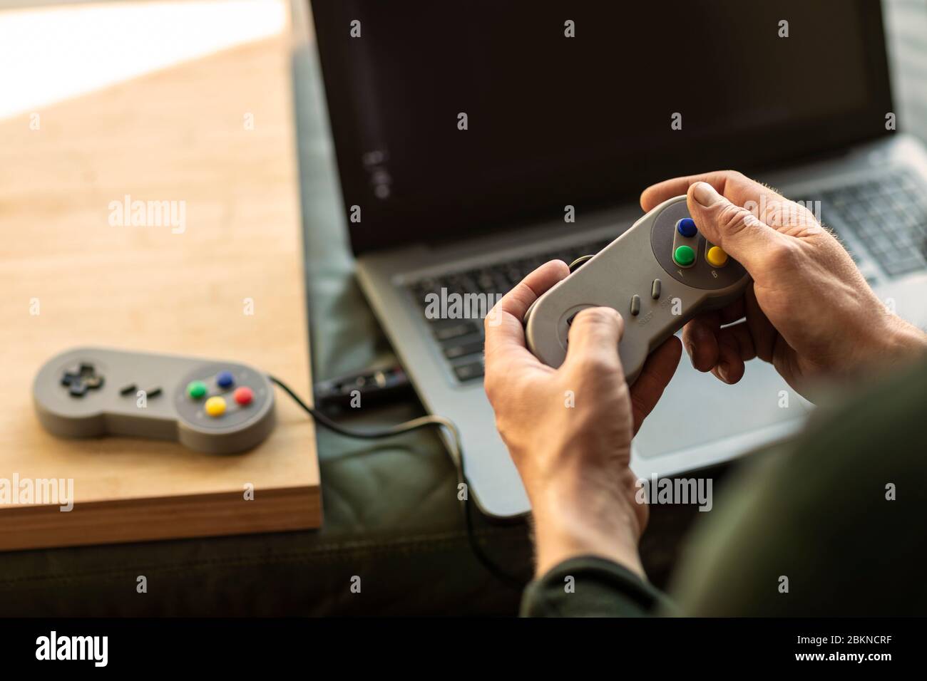 Un uomo che gioca sul suo computer portatile con una classica console di gioco della vecchia scuola sentendosi nostalgico a casa durante il periodo di blocco nel 2020 Foto Stock