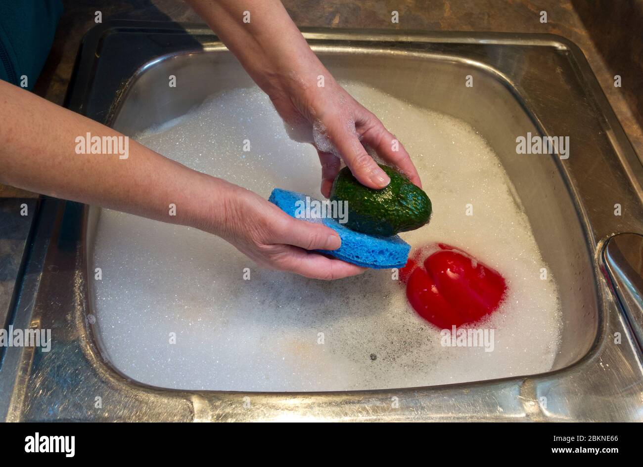 Donna che lava le verdure nel lavello della cucina con sapone piatto, cosa che NON è consigliata. Pulizia delle verdure (in modo errato) a causa della pandemia del coronavirus Foto Stock