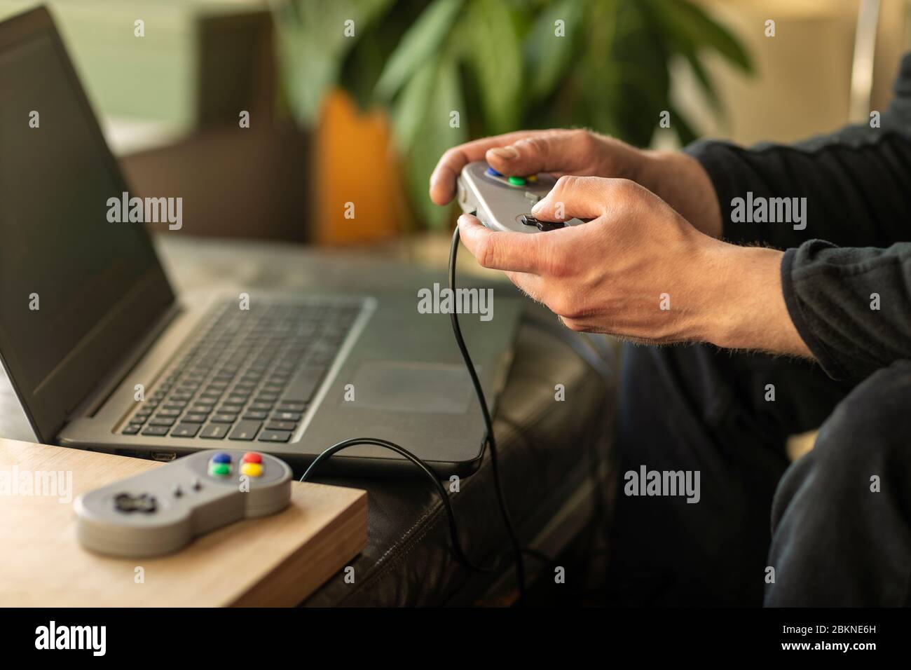 Un uomo che gioca sul suo computer portatile con una console di gioco classica vecchia scuola sentendosi nostalgico a casa durante il periodo di blocco nel 2020 Foto Stock