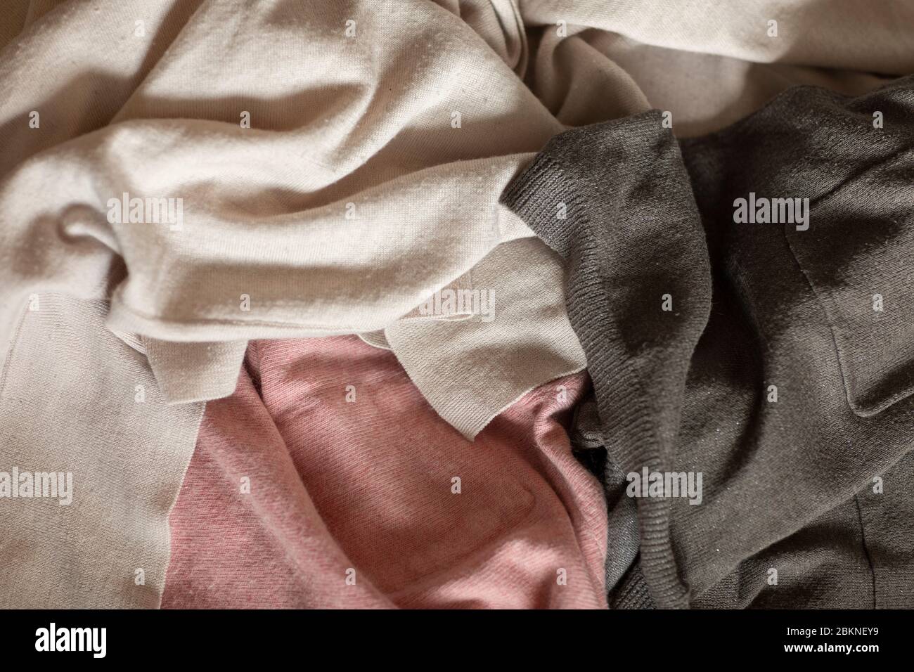 Vecchi abiti in rosa e grigio su un mucchio. Pezzi usurati con pillole e polsini in diversi materiali pronti per essere riciclati, circolare economia Foto Stock