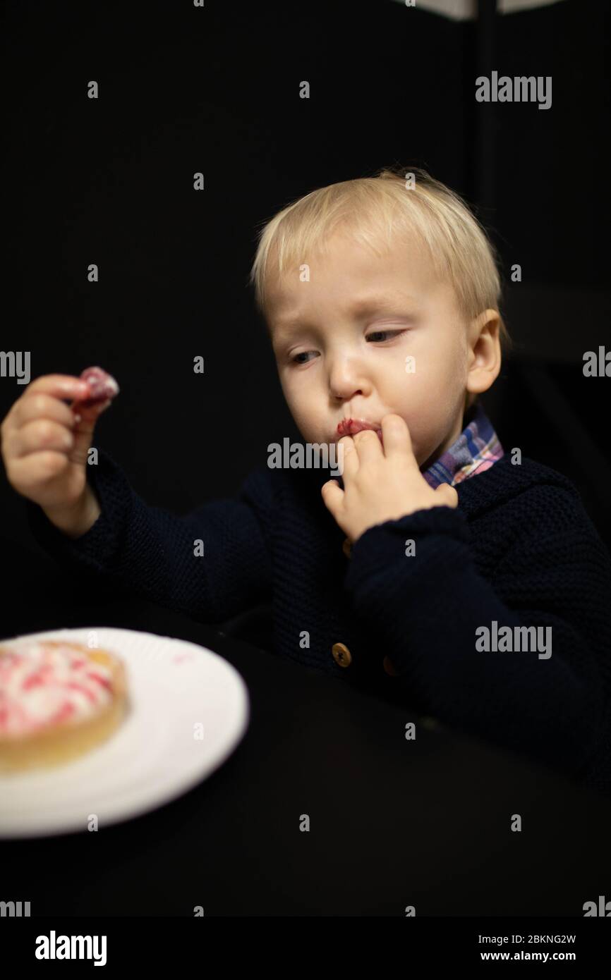 Un ragazzino biondo mangia dolci. Delizioso tartlet. Foto Stock