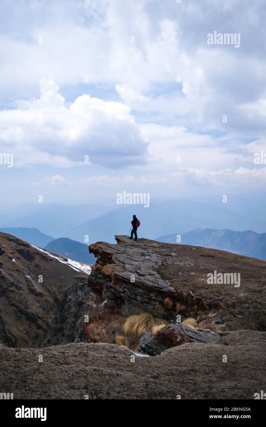 Vista lontana di un giovane escursionista indiano con zaino in piedi al bordo di una scogliera di montagna Foto Stock