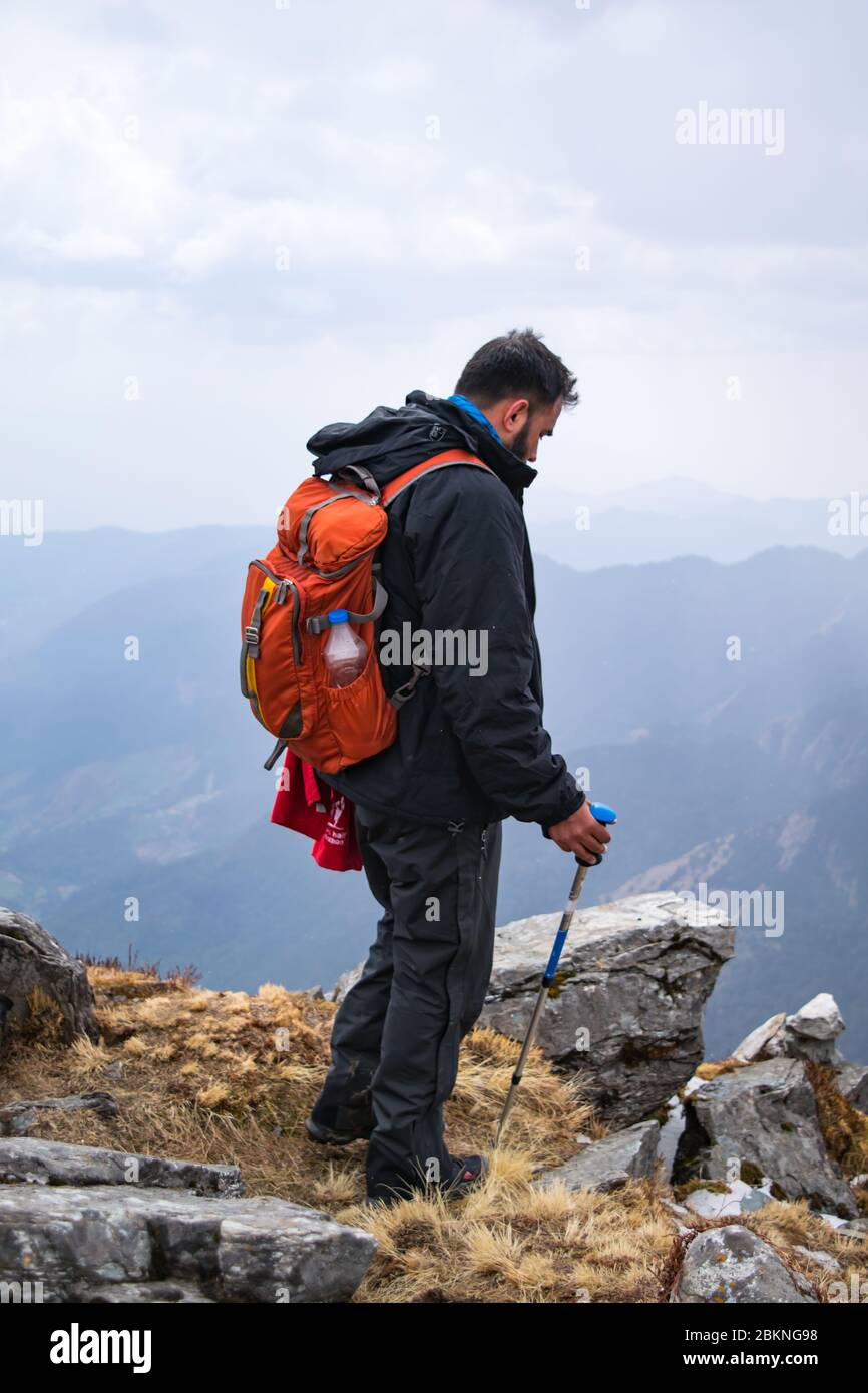 Vista posteriore di un giovane escursionista indiano con zaino in piedi al bordo di una scogliera di montagna Foto Stock