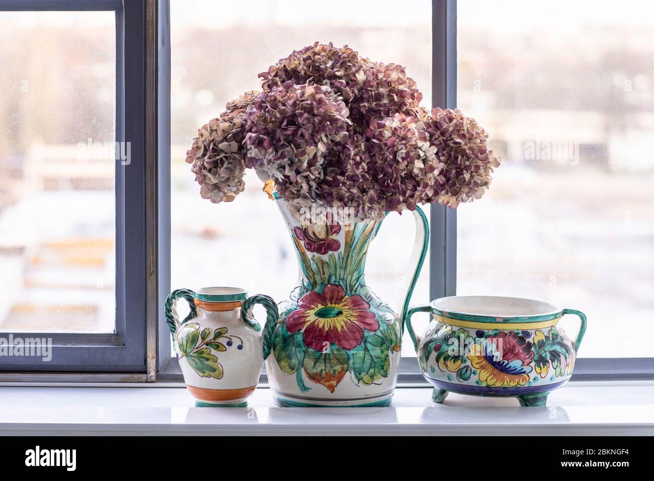 Un set di vasi e pentole in ceramica dipinta in un interno loft cittadino. Una casa bohémien, moderna, mix e si abbina eclettico stile casa con un fiori secchi di fronte Foto Stock