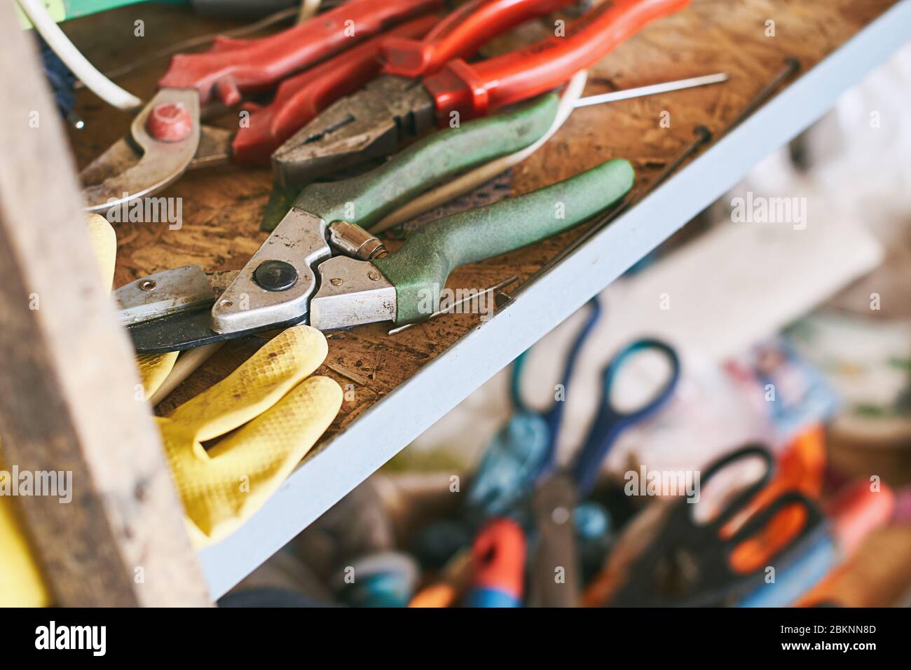 Strumenti vecchi come tagliafili, pinze diagonali, forbici da giardino e guanti da lavoro su uno scaffale in garage Foto Stock