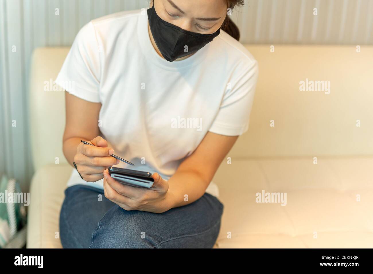 Donna in maschera protettiva che lavora sullo smartphone utilizzando la penna digitale Foto Stock