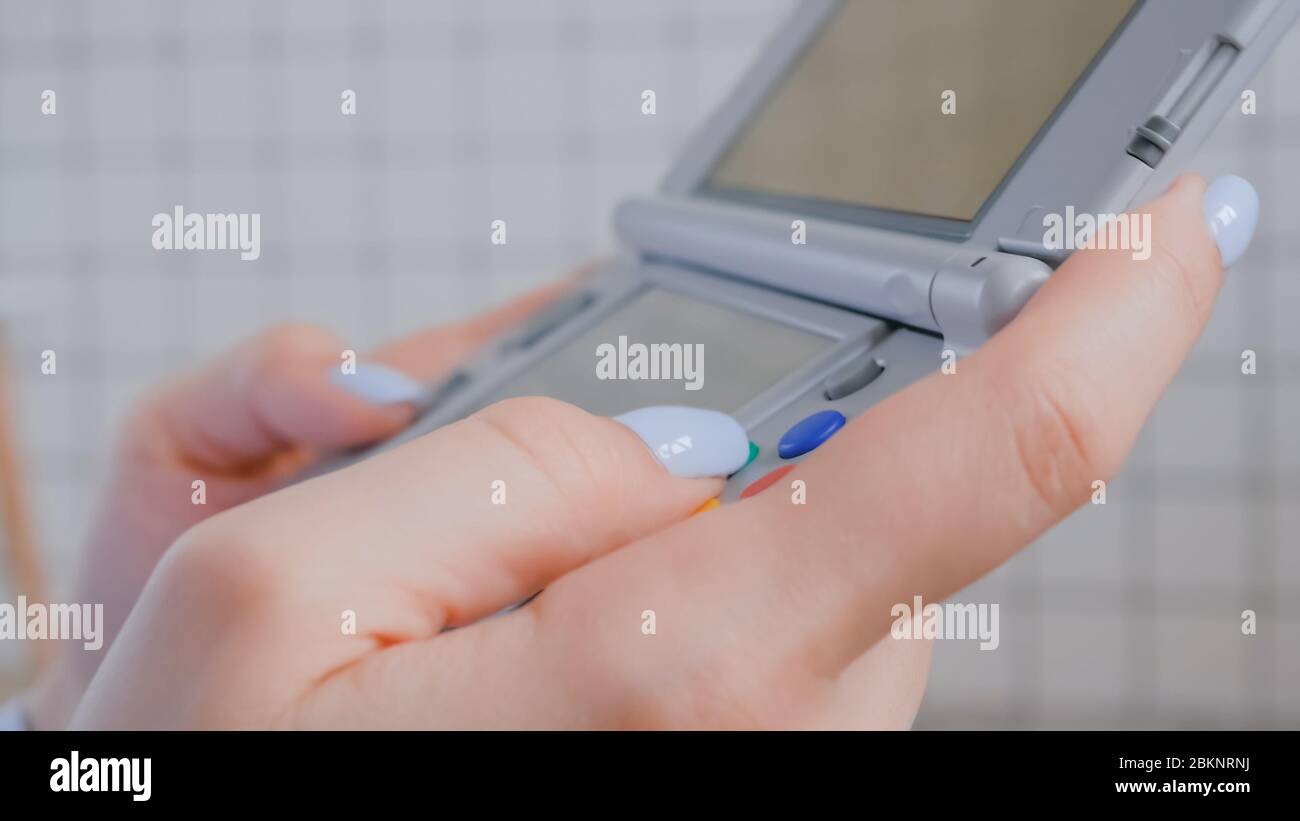 Vista ravvicinata della mano di una donna gamer utilizzando la console di gioco portatile grigia a casa. Giochi, hobby, tecnologia, intrattenimento, portatile, videogiochi e tempo libero Foto Stock