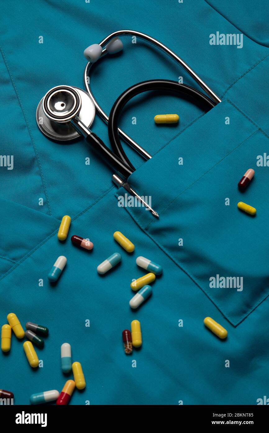 Stetoscopio e pillole su fondo blu di cappotto medico. Concetto di medicina e sanità Foto Stock