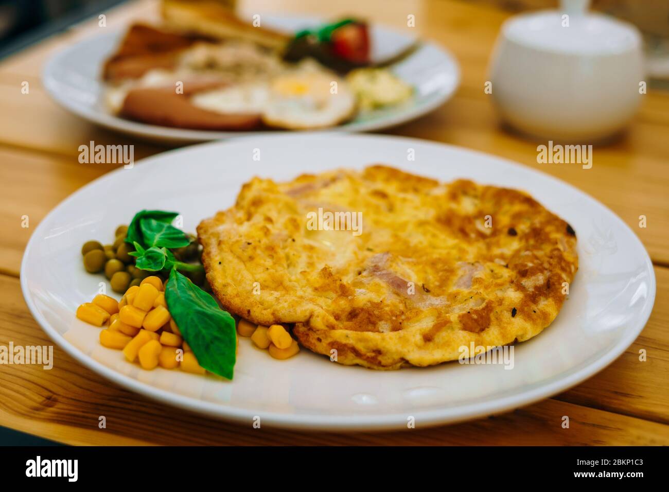 Frittata con prosciutto, piselli e mais in un bar. Deliziosa colazione con omelette, formaggio e piselli. Frittata con verdure su un piatto bianco in un accogliente caffè Foto Stock